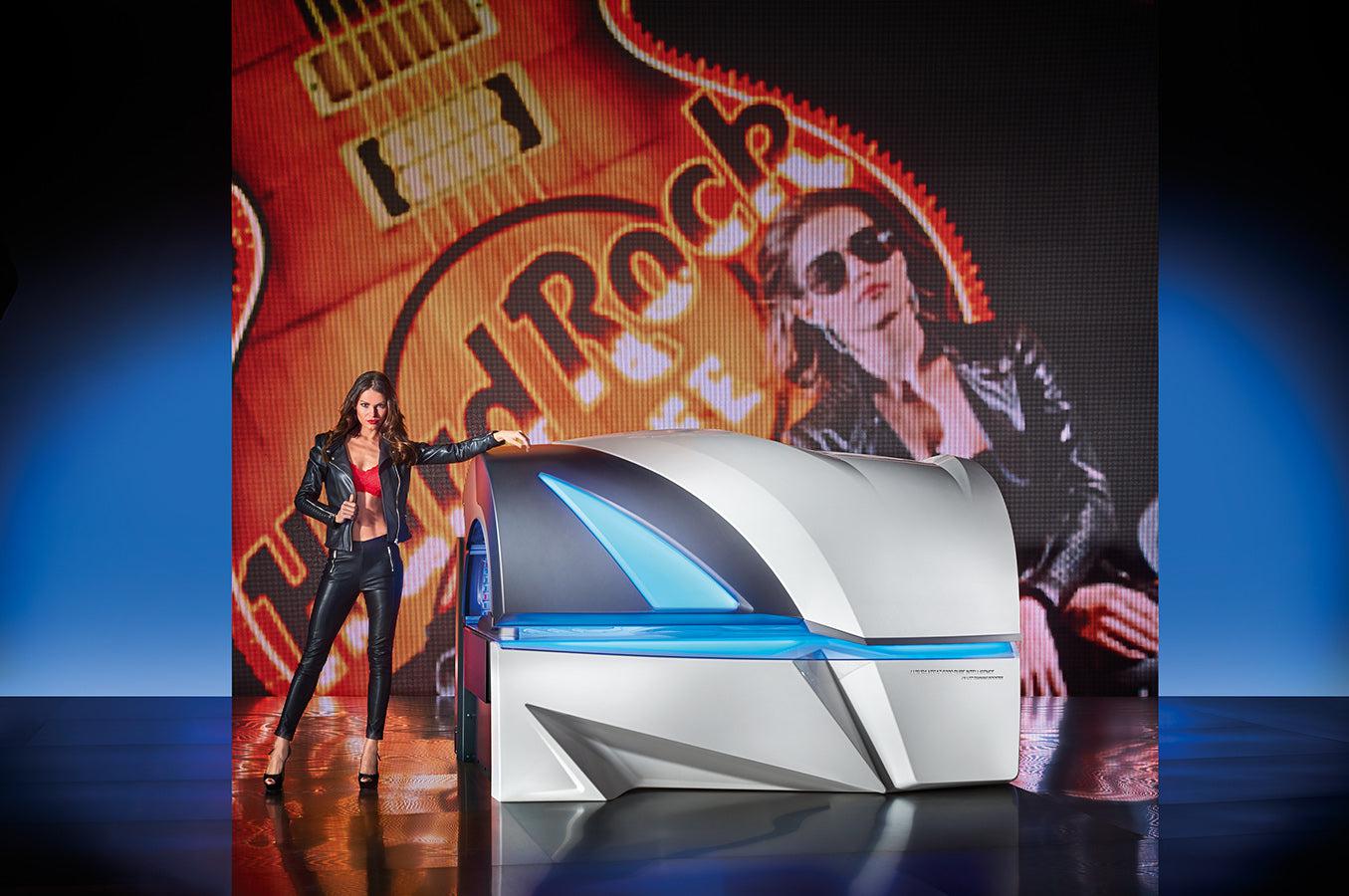 A professional tanning bed with a metal and glass design, featuring a image of a woman on stage at a rock concert, and a blue light illuminating the surrounding area.